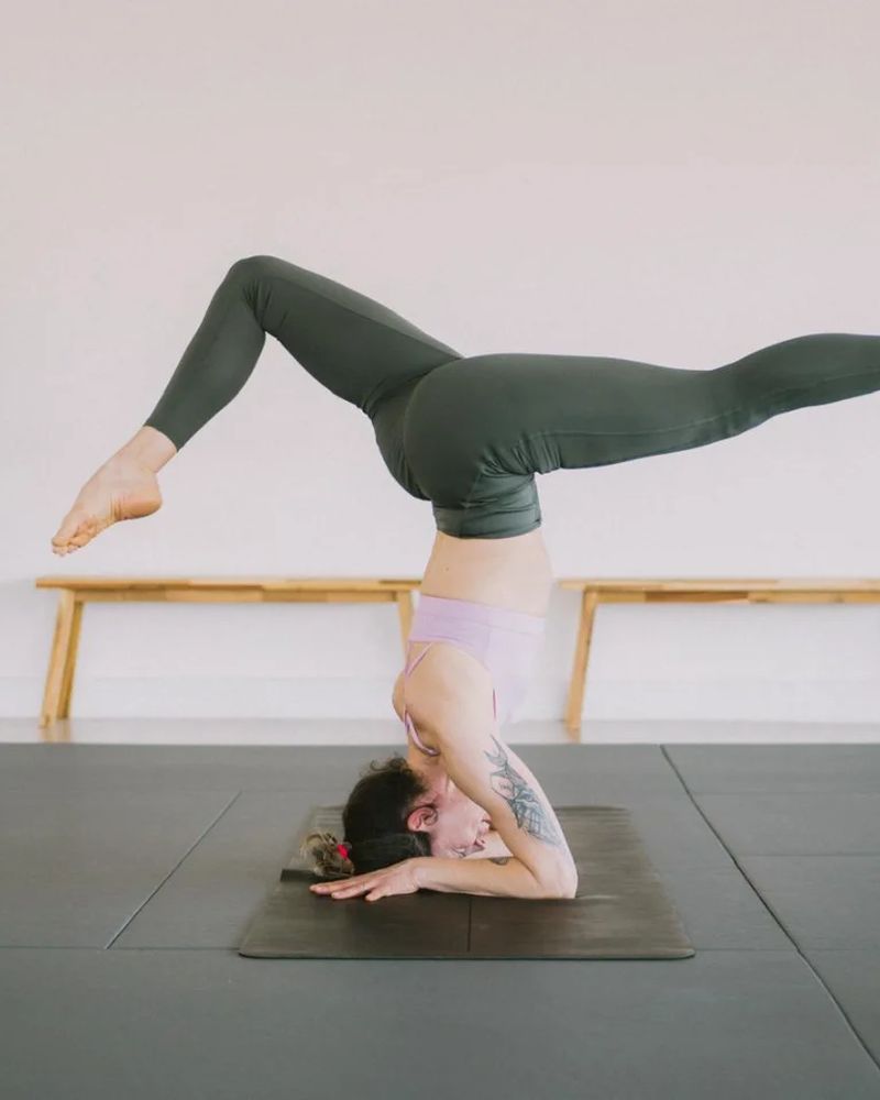 A forearm balance with both legs open, beside the studio plant