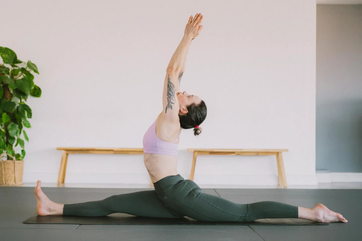 A seated split with one arm reaching up, in the studio